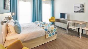 A modern hotel room with a bed, a desk, a chair, and a television.
