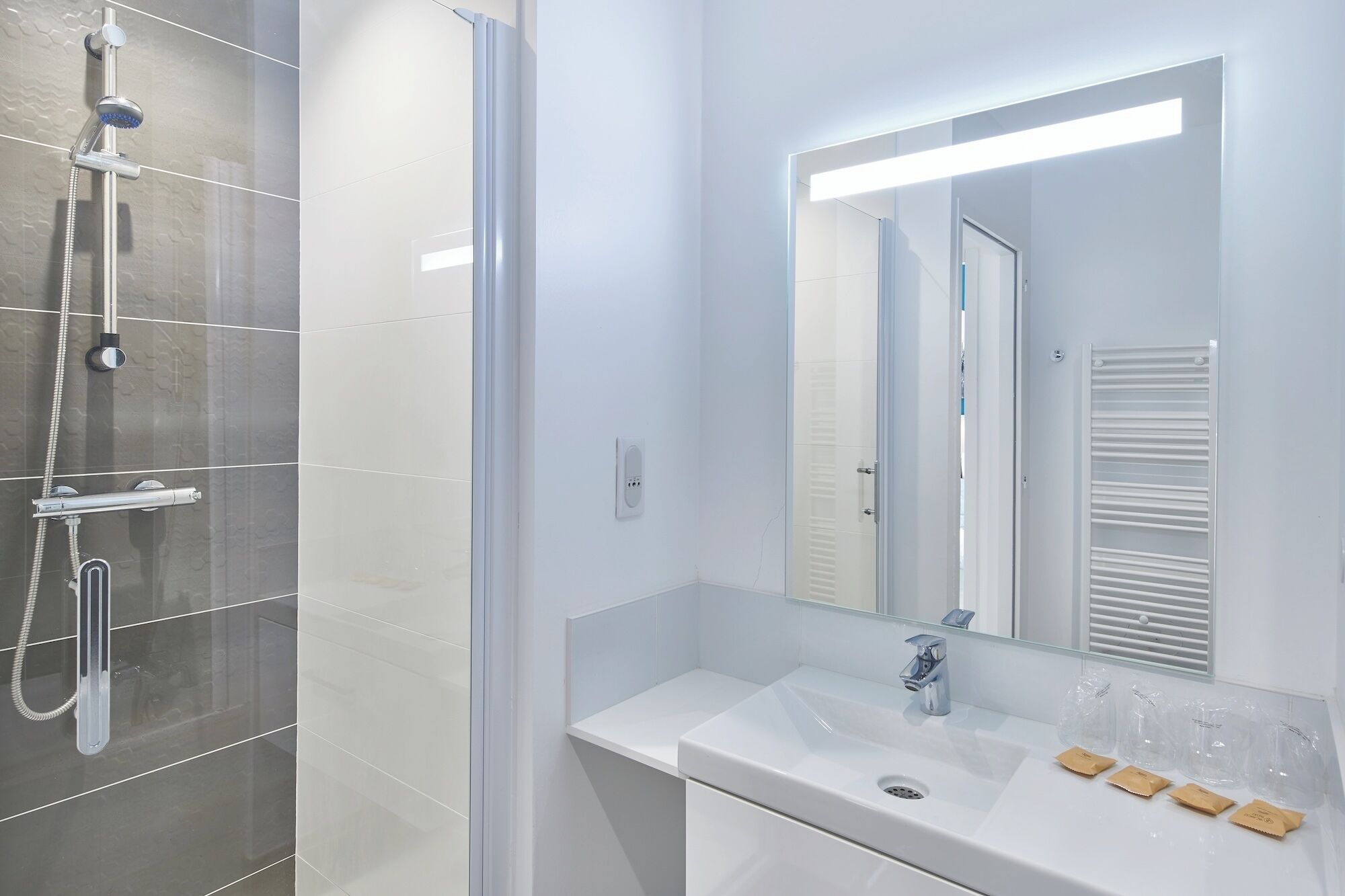 Een moderne badkamer met een douchecabine van glas, een witte wastafel met spiegel en een handdoekrek.