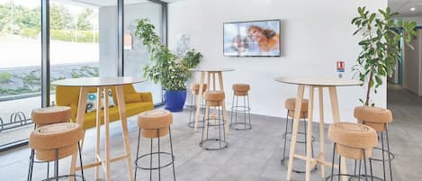 A modern interior with round tables and stools, large windows, and indoor plants.