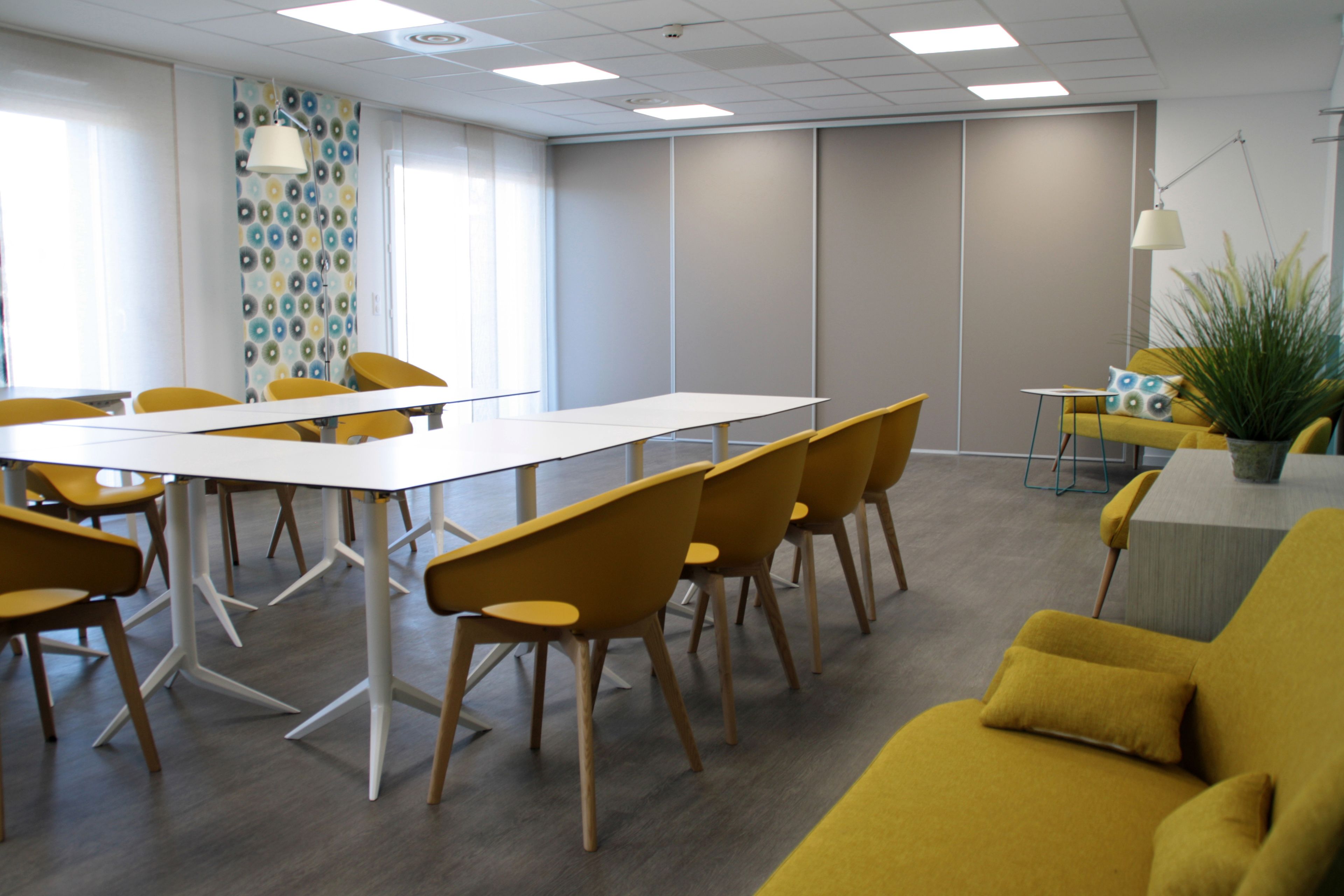 Una sala de reuniones moderna con una larga mesa, sillas amarillas, un sofá y una planta en maceta.