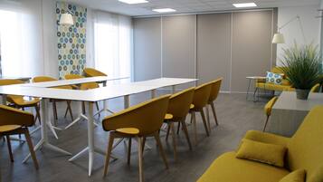 Una sala de reuniones moderna con una larga mesa, sillas amarillas, un sofá y una planta en maceta.