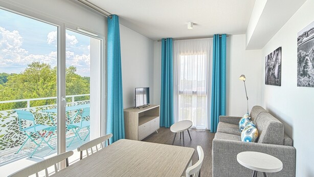 Una habitación moderna con balcón, zona de comedor, sofá y televisor.