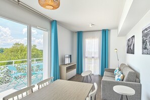 A modern room with a balcony, a dining area, a sofa, and a TV. -  Résidence Vacances Bleues Les Coteaux de Jonzac (Jonzac)