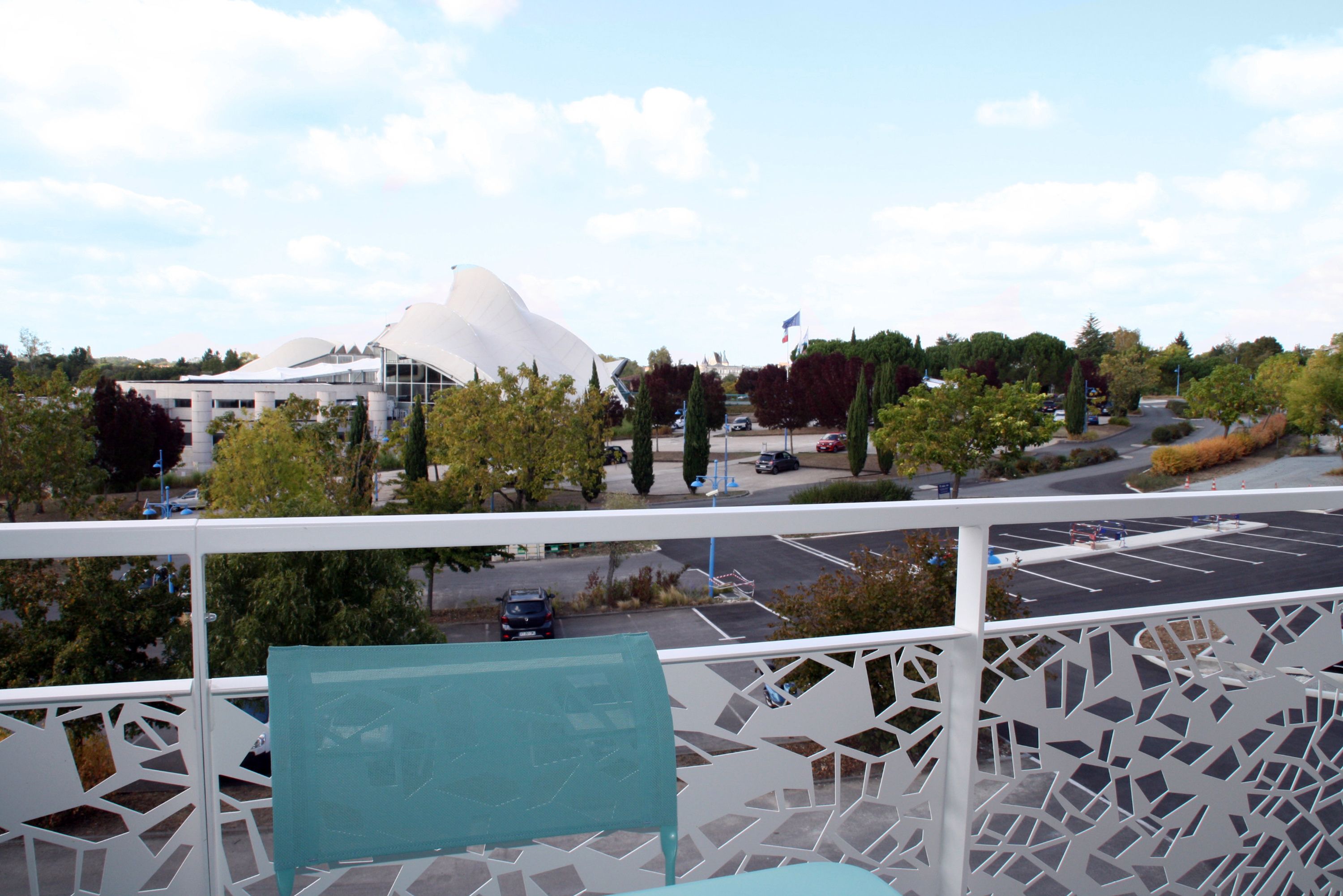 A balcony with a view of a modern building and a parking lot.