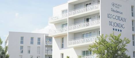 A multi-story hotel with balconies, a sign indicating it is a vacation property, and a name that suggests a location in De Jonzac.