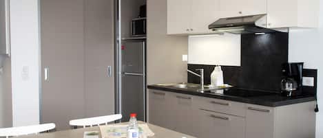 Cocina compacta con microondas, refrigerador y cafetera. Hay una mesa de comedor con sillas y una botella de agua.