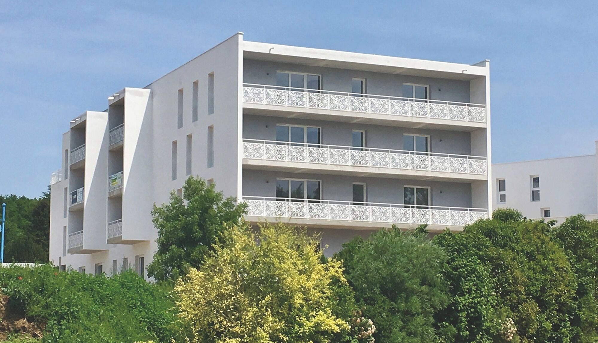 A multi-story residential building with balconies, surrounded by greenery.