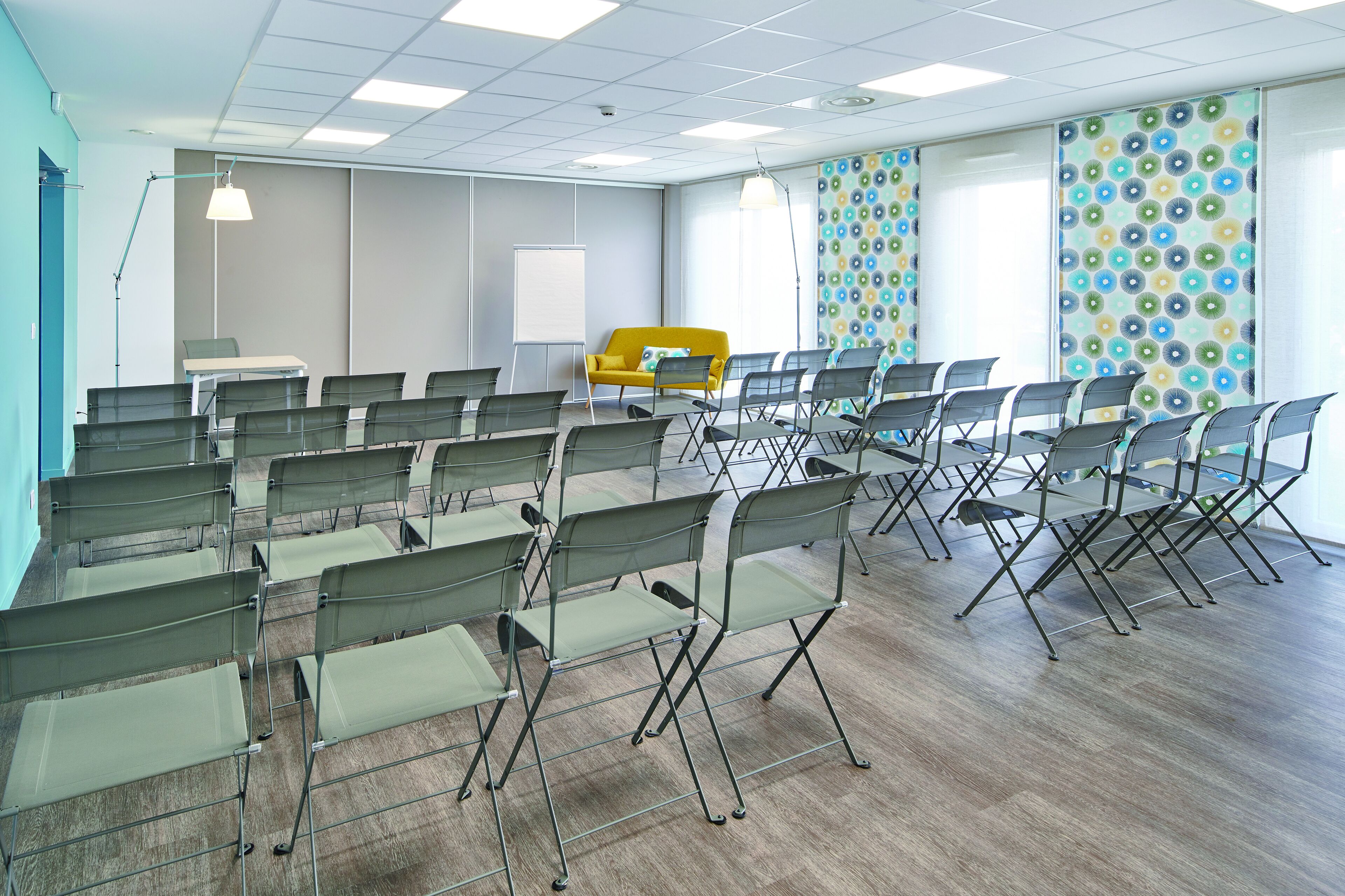 A conference room with rows of foldable chairs, a whiteboard, and a yellow sofa.