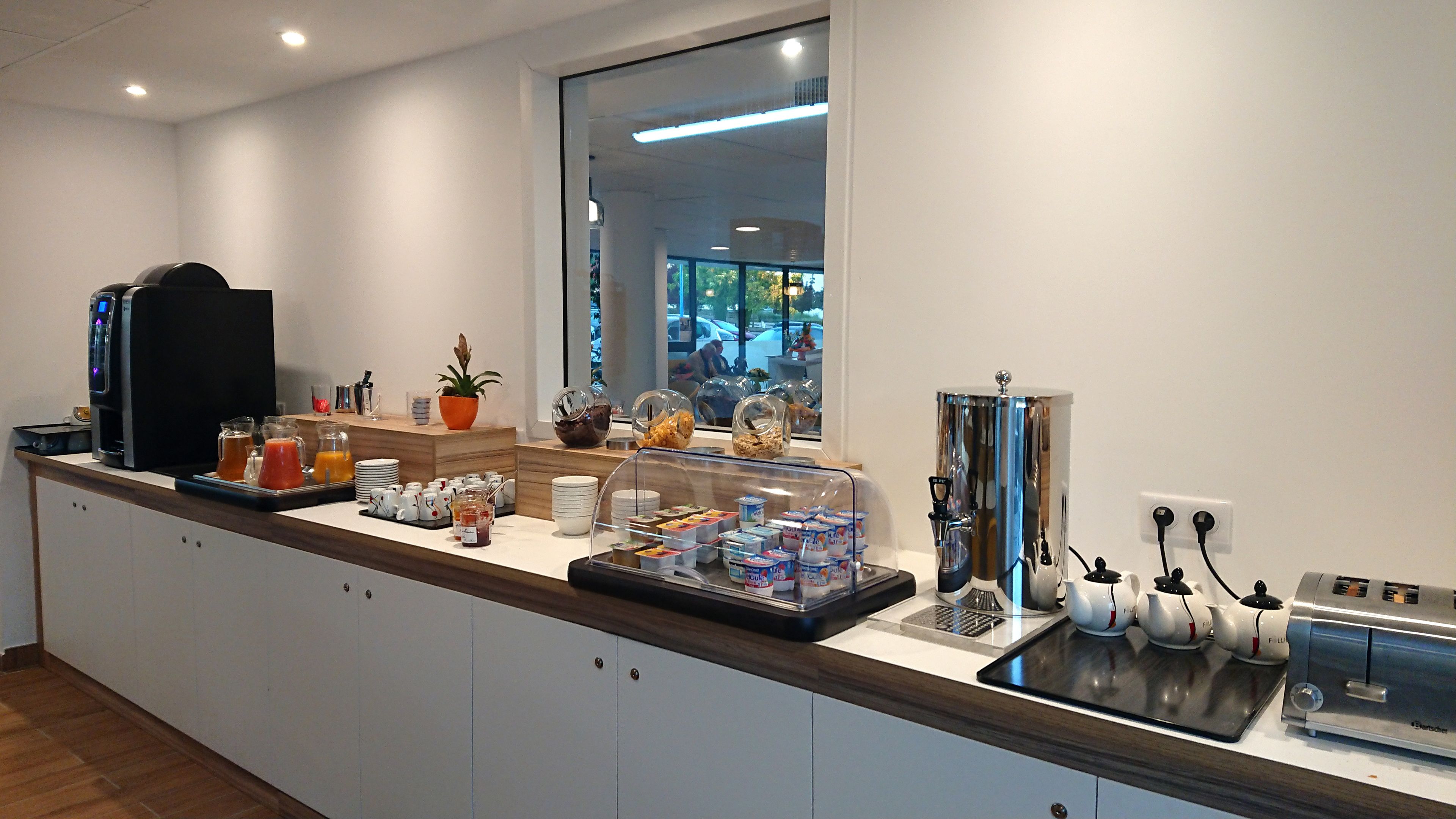 A breakfast bar with coffee machines, a fruit bowl, and various food items.