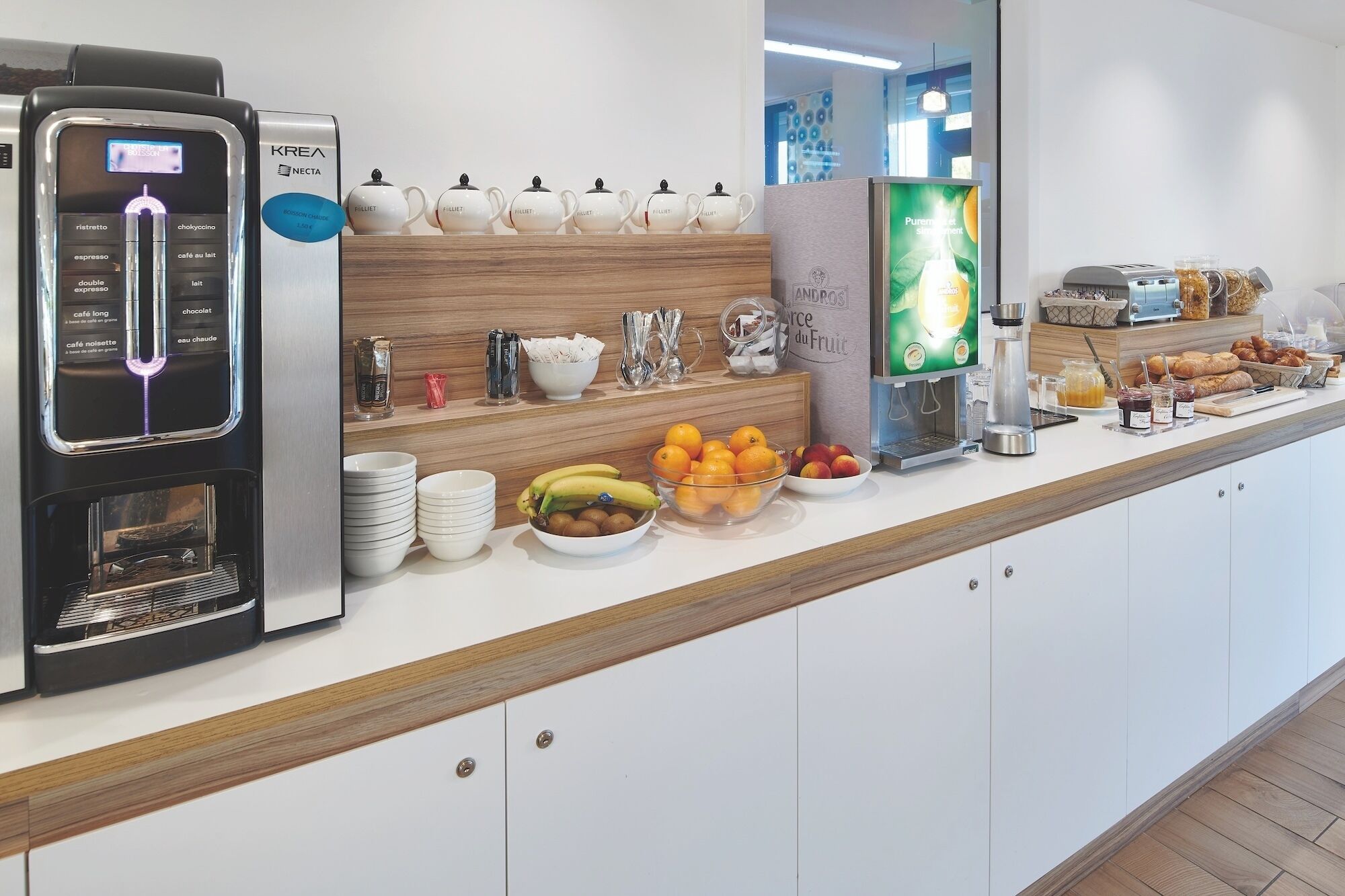 A buffet setup with a coffee machine, tea pots, fruit bowls, and a juice dispenser.