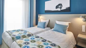 A hotel room with two beds, a nightstand, a wall-mounted lamp, and a painting of a tree.