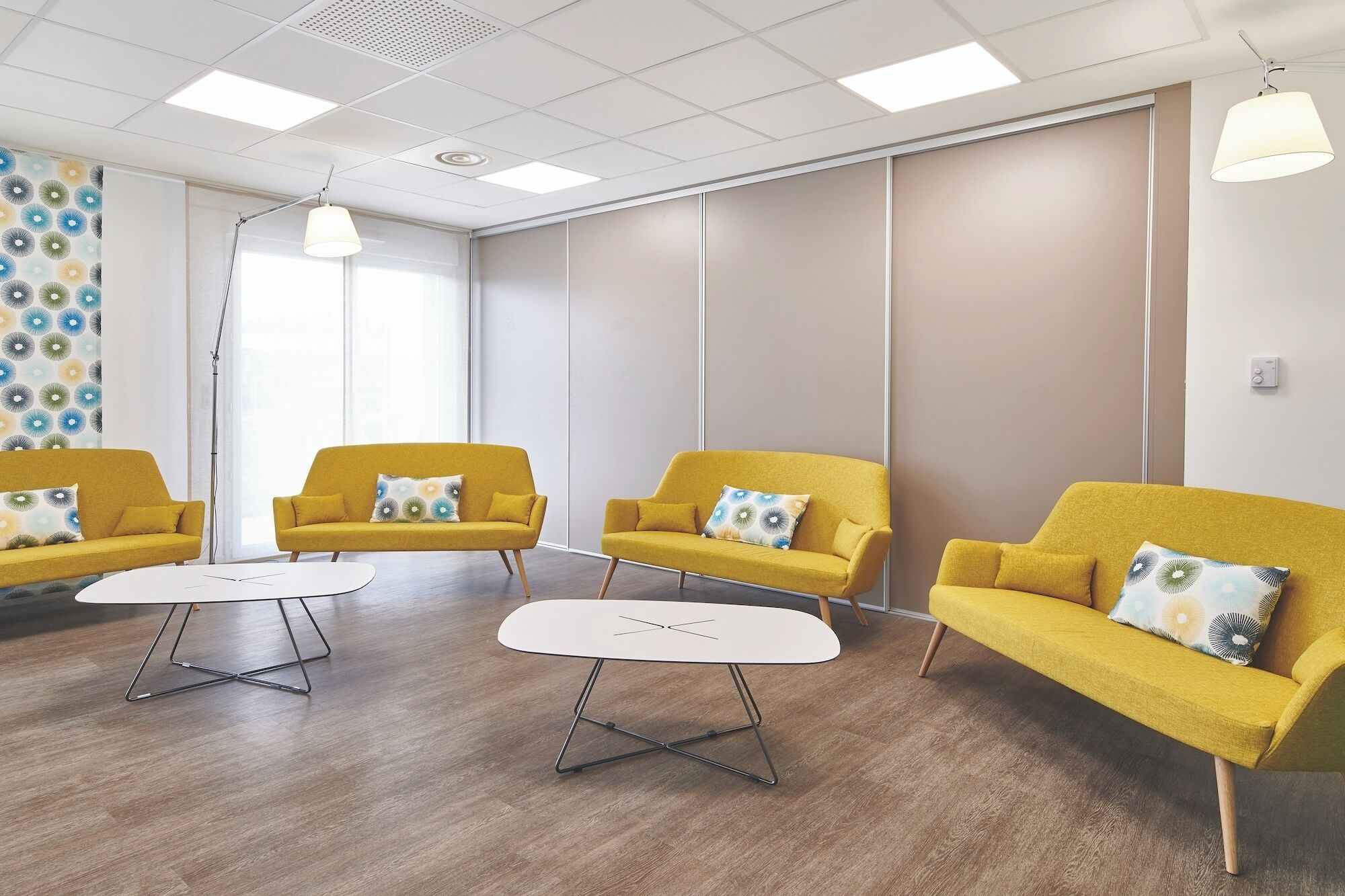 Ein Zimmer mit drei gelben Sofas, einem weißen Tisch und einer Wand mit Muster.