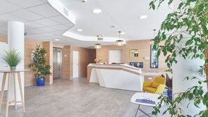 Un área de recepción moderna con un mostrador curvo, una silla amarilla y plantas en macetas.