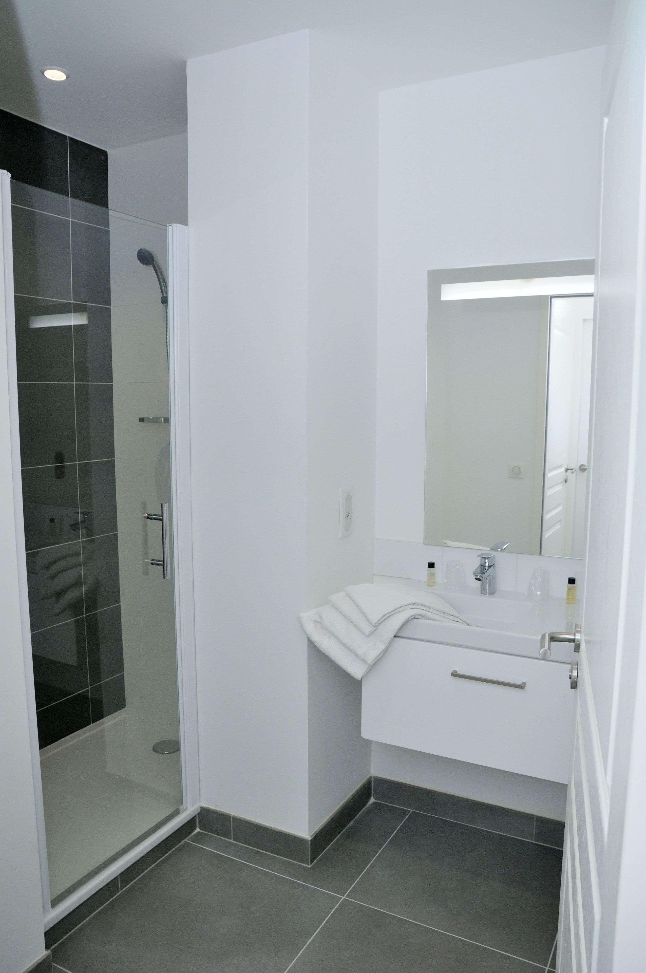 Ein modernes Badezimmer mit einer gläsernen Duschkabine, einem weißen Waschbecken und einem Spiegel sowie einem gefliesten Boden.