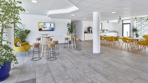 Un moderno vestíbulo de hotel con una mesa redonda, sillas amarillas y plantas en macetas.