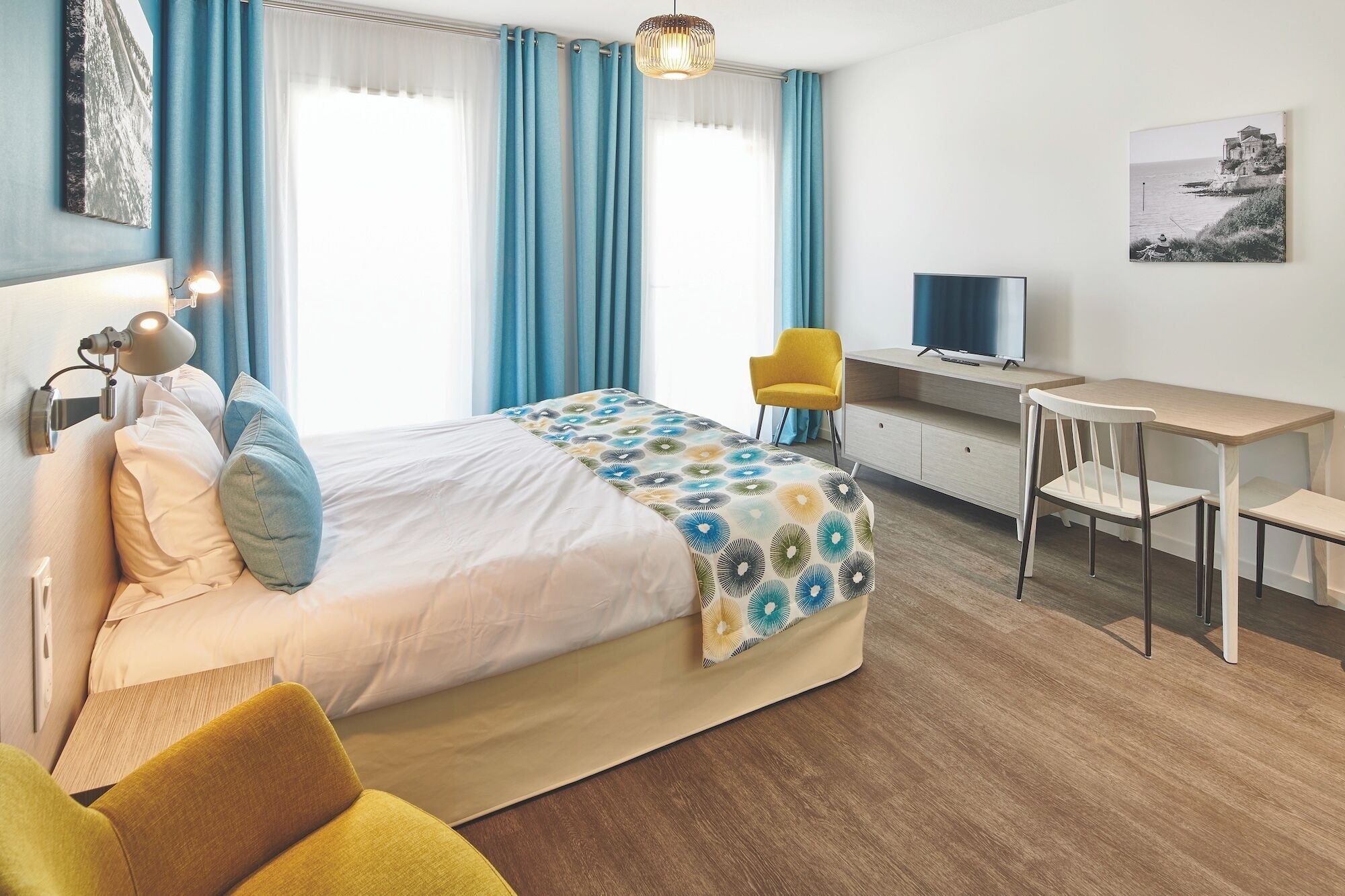 A bedroom with a bed, a desk, a chair, a TV, and a painting on the wall.