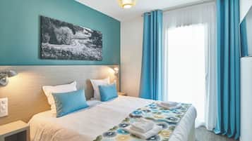 Quarto de hotel com cama, mesa de cabeceira, luminária na parede, um quadro e janela com cortinas.