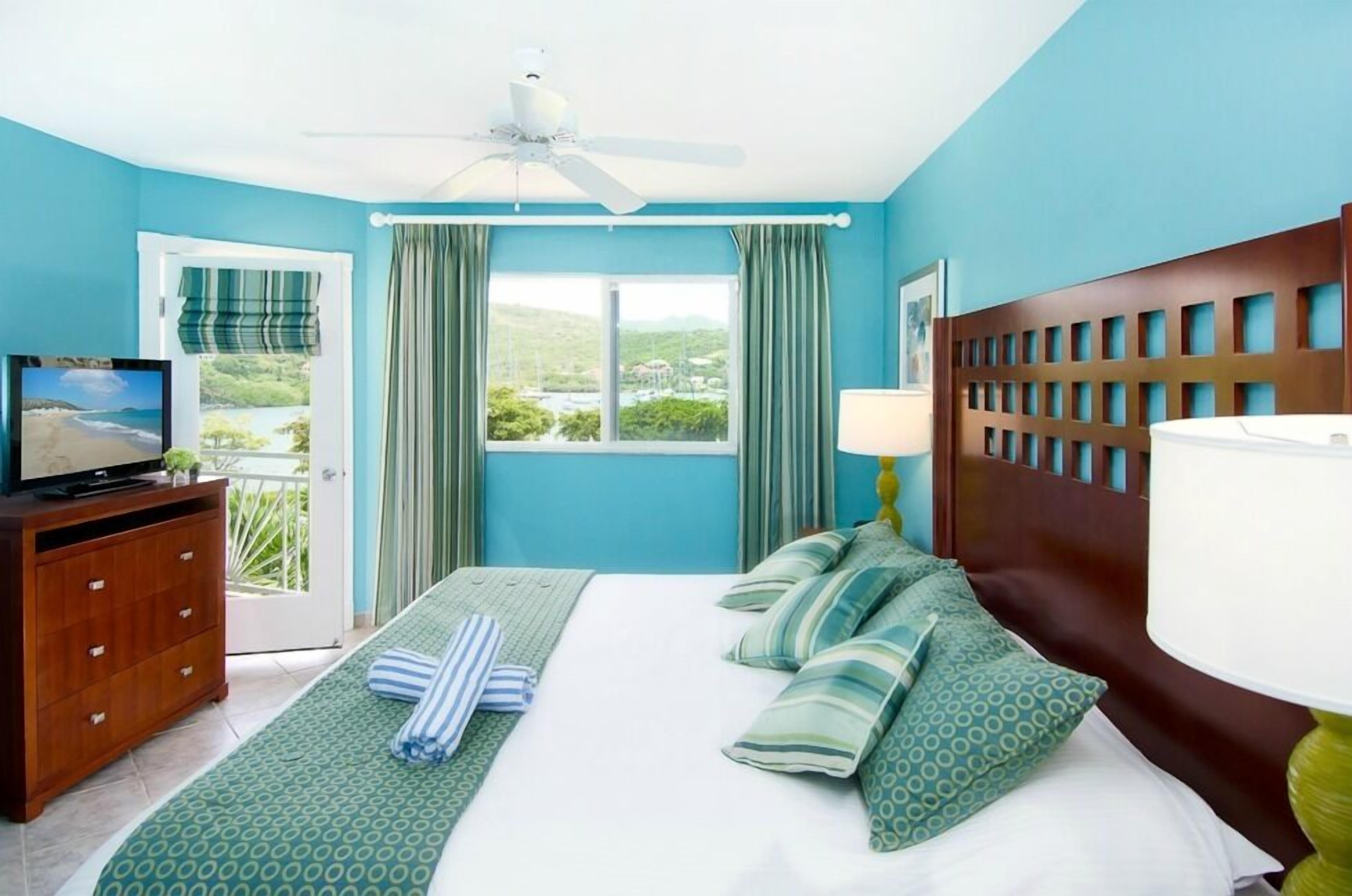 A hotel room with a bed, a TV, a dresser, and a window with curtains.