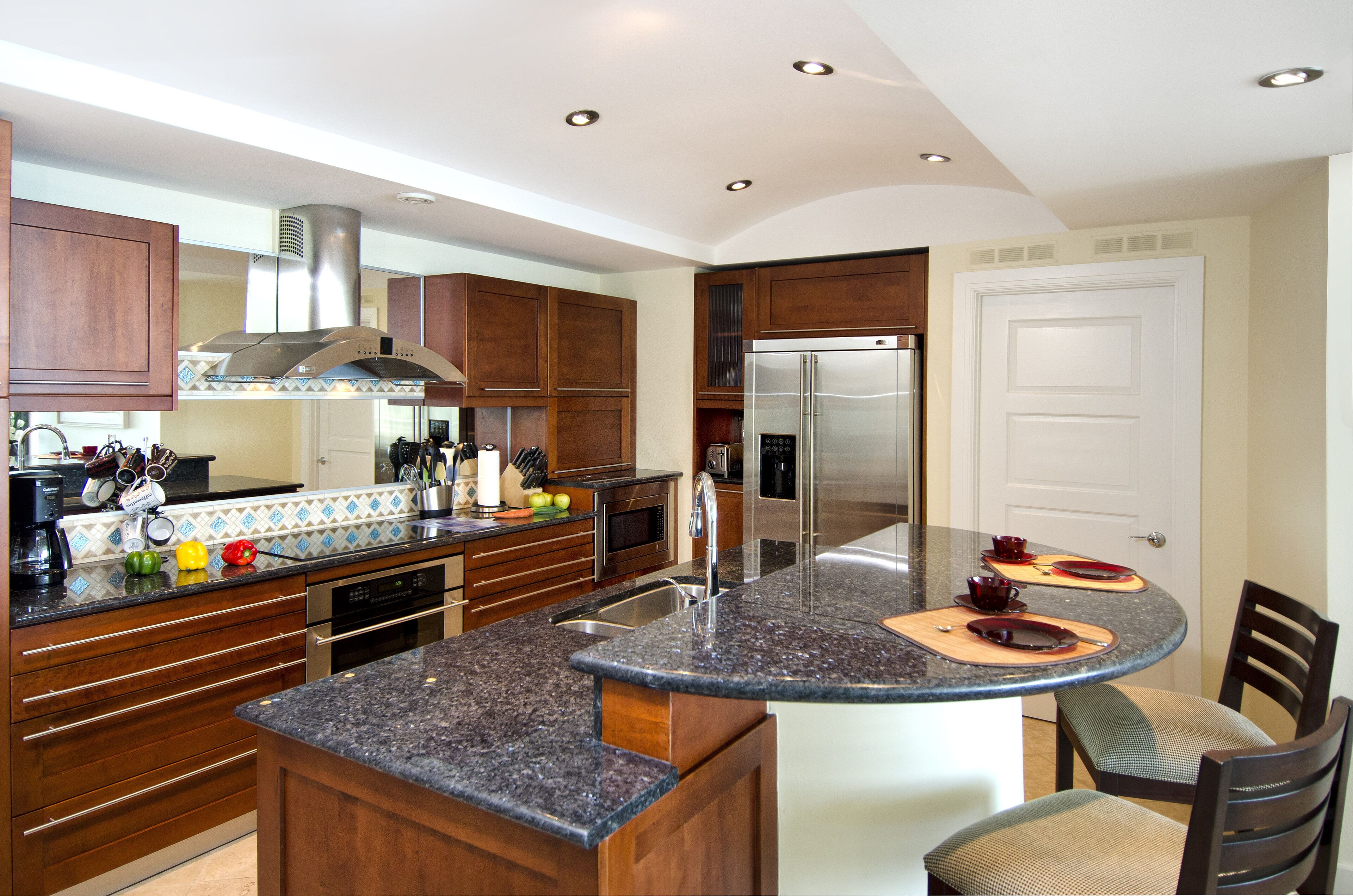 A modern kitchen with wooden cabinets, a granite countertop, stainless steel appliances, and a built-in island with seating.