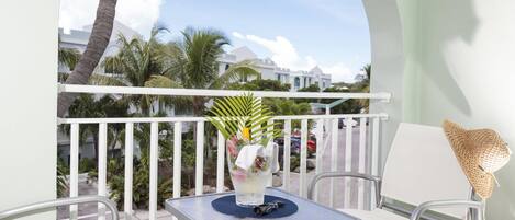 A balcony with a table and two chairs, a decorative vase with flowers, and a view of palm trees and buildings.