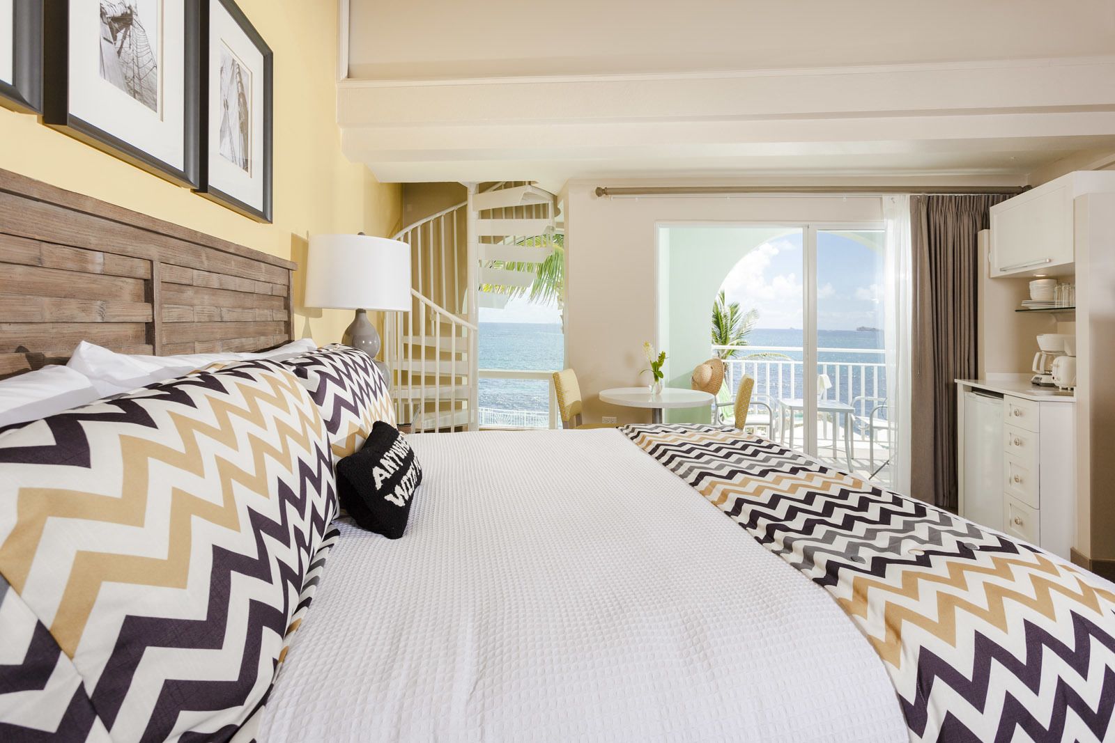 A hotel room with a large bed, a balcony with a view of the ocean, and a staircase leading to an upper level.