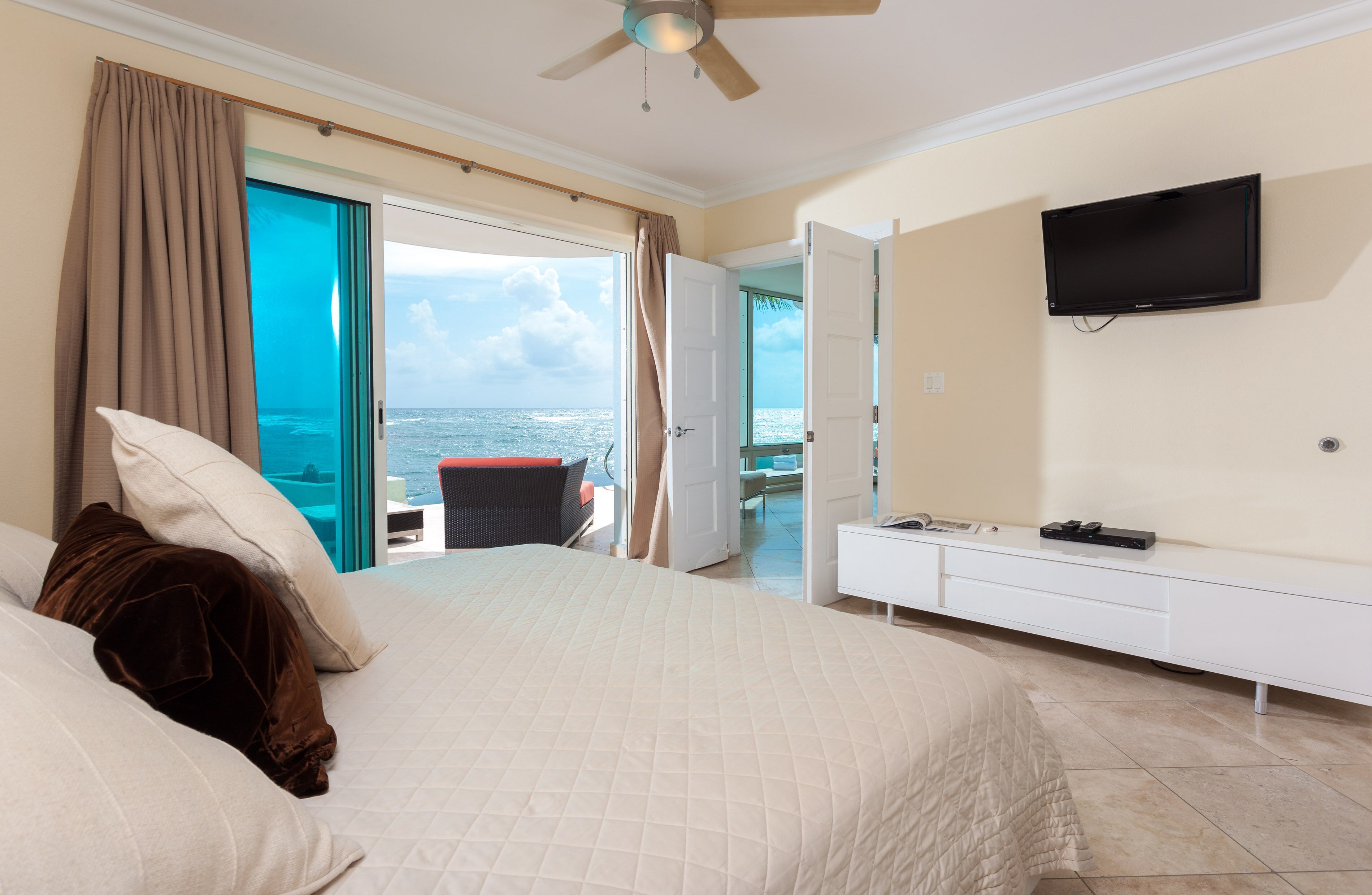 A hotel room with a bed, a TV, a desk, and a view of the ocean.