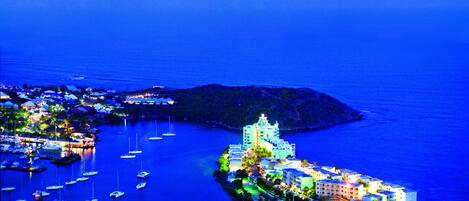 A coastal town with a prominent hotel featuring a central tower, surrounded by smaller buildings and a marina with boats.