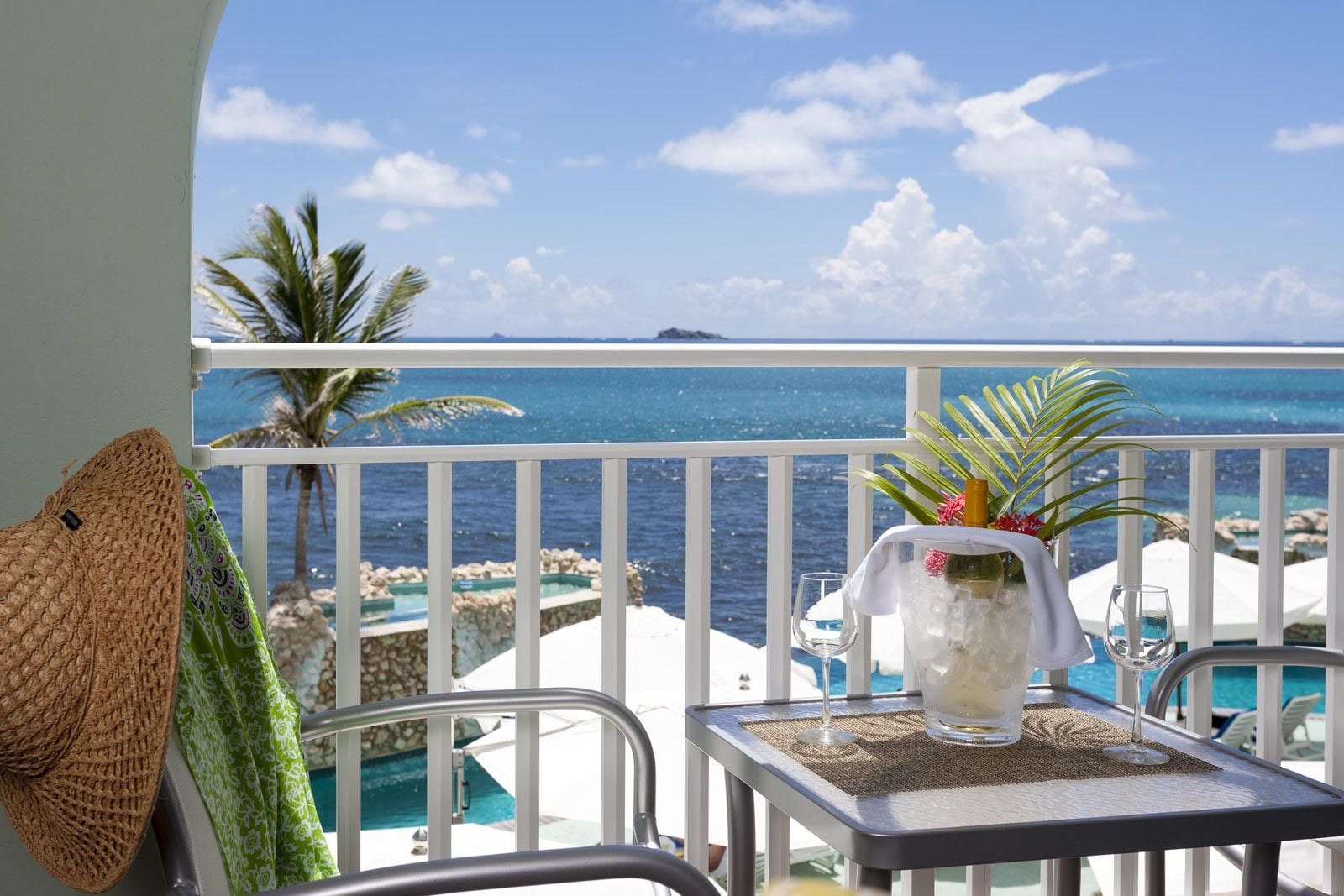 A balcony with a view of the ocean, a table with a glass of water, a woven basket, and a potted plant.