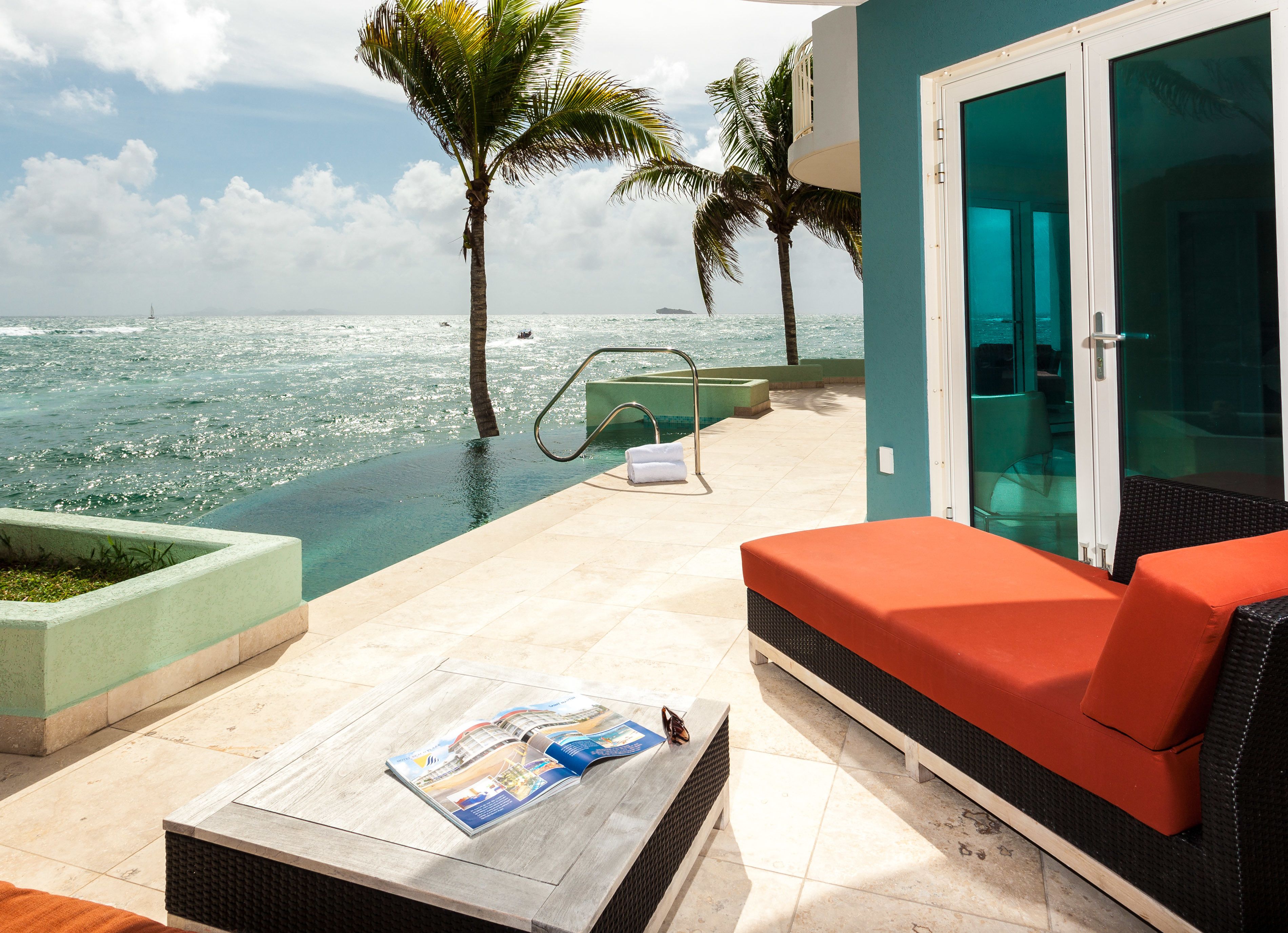 Zona de piscina con una silla de descanso, una revista sobre una mesa y vista al océano.