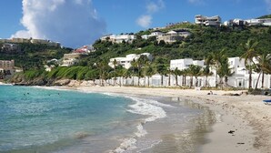 A beach with clear turquoise water, a sandy shore, and white buildings on a hillside.