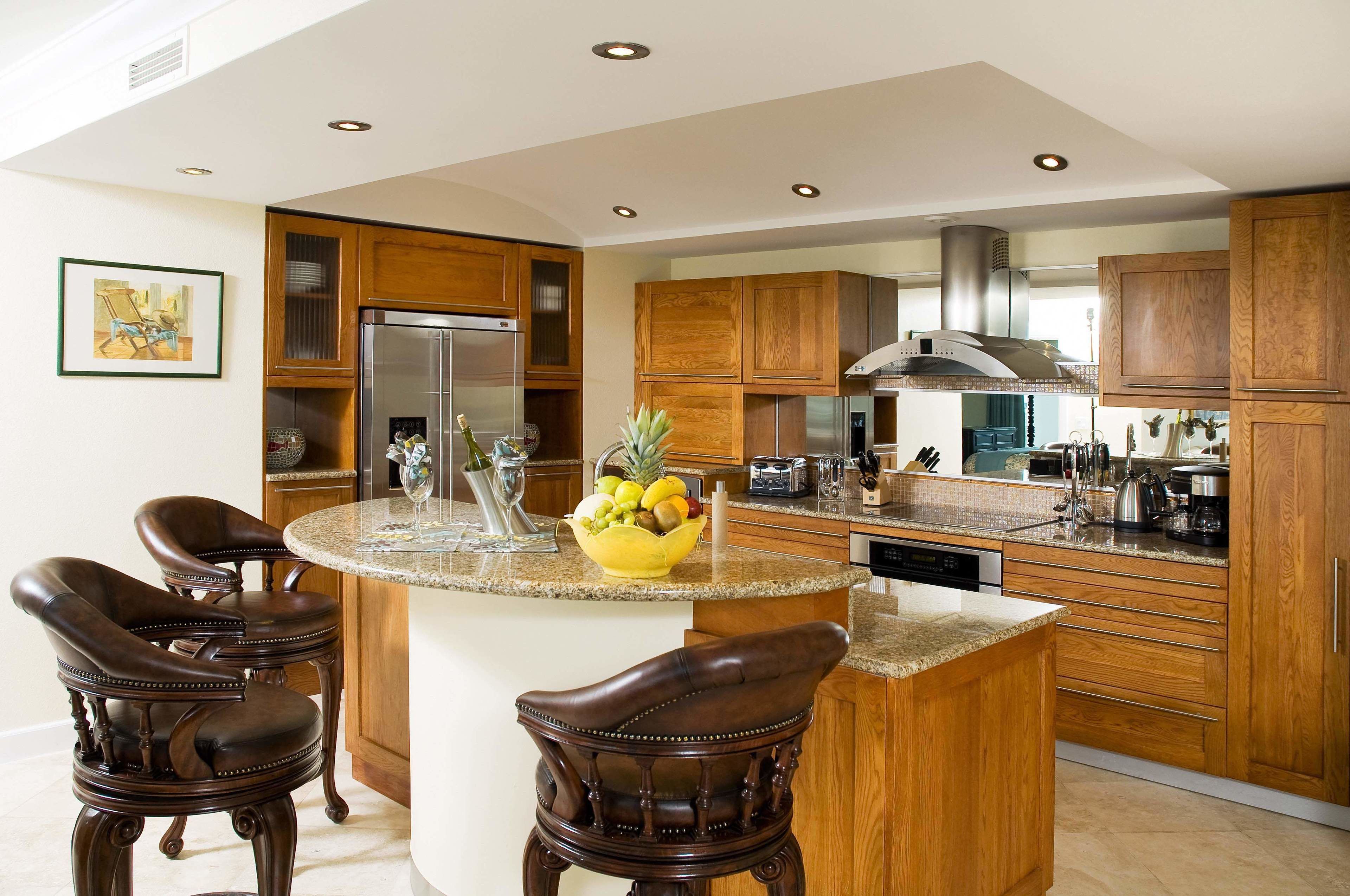 A modern kitchen with wooden cabinets, a central island with bar stools, a stainless steel refrigerator, and a variety of kitchen appliances.