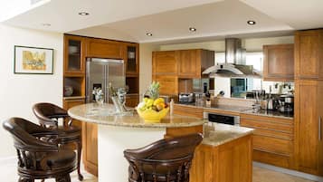 A modern kitchen with wooden cabinets, a central island with bar stools, a stainless steel refrigerator, and a variety of kitchen appliances.