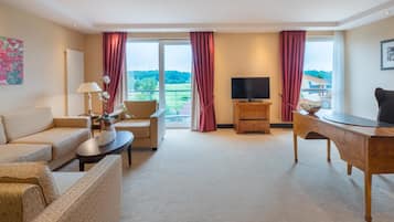 Et hotelværelse med sofa, lænestol, fjernsyn, skrivebord og udsigt til det fri.