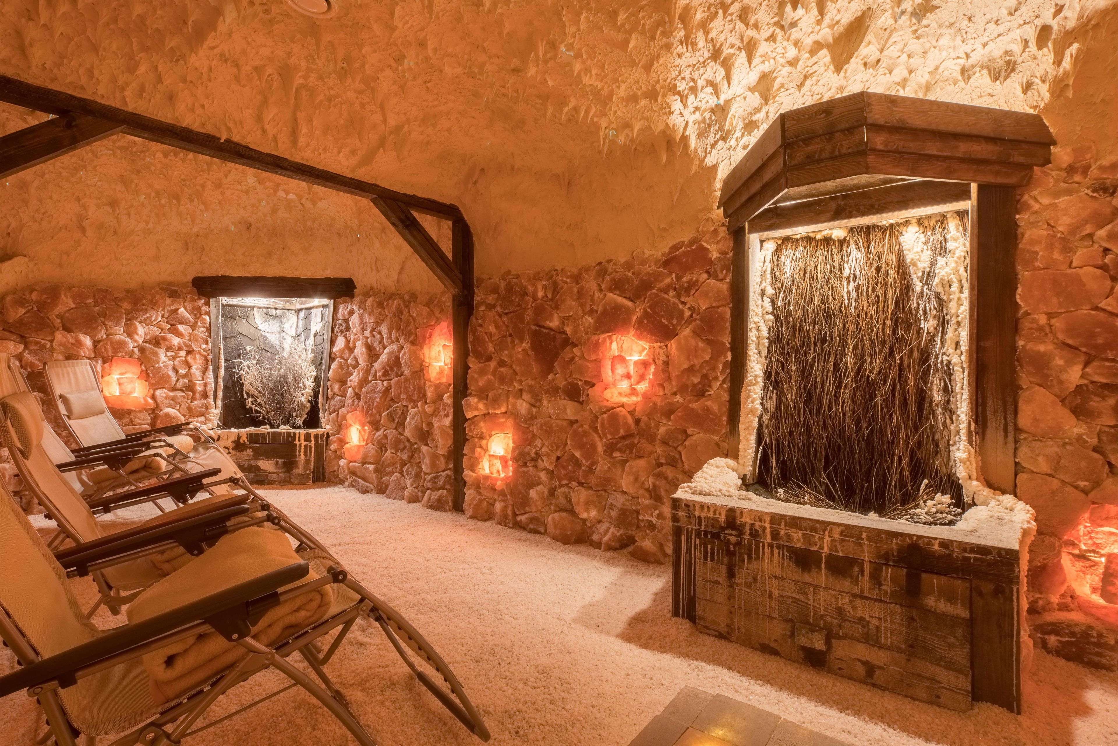 Una habitación con paredes de piedra, una chimenea, un sillón y una pequeña mesa con velas.