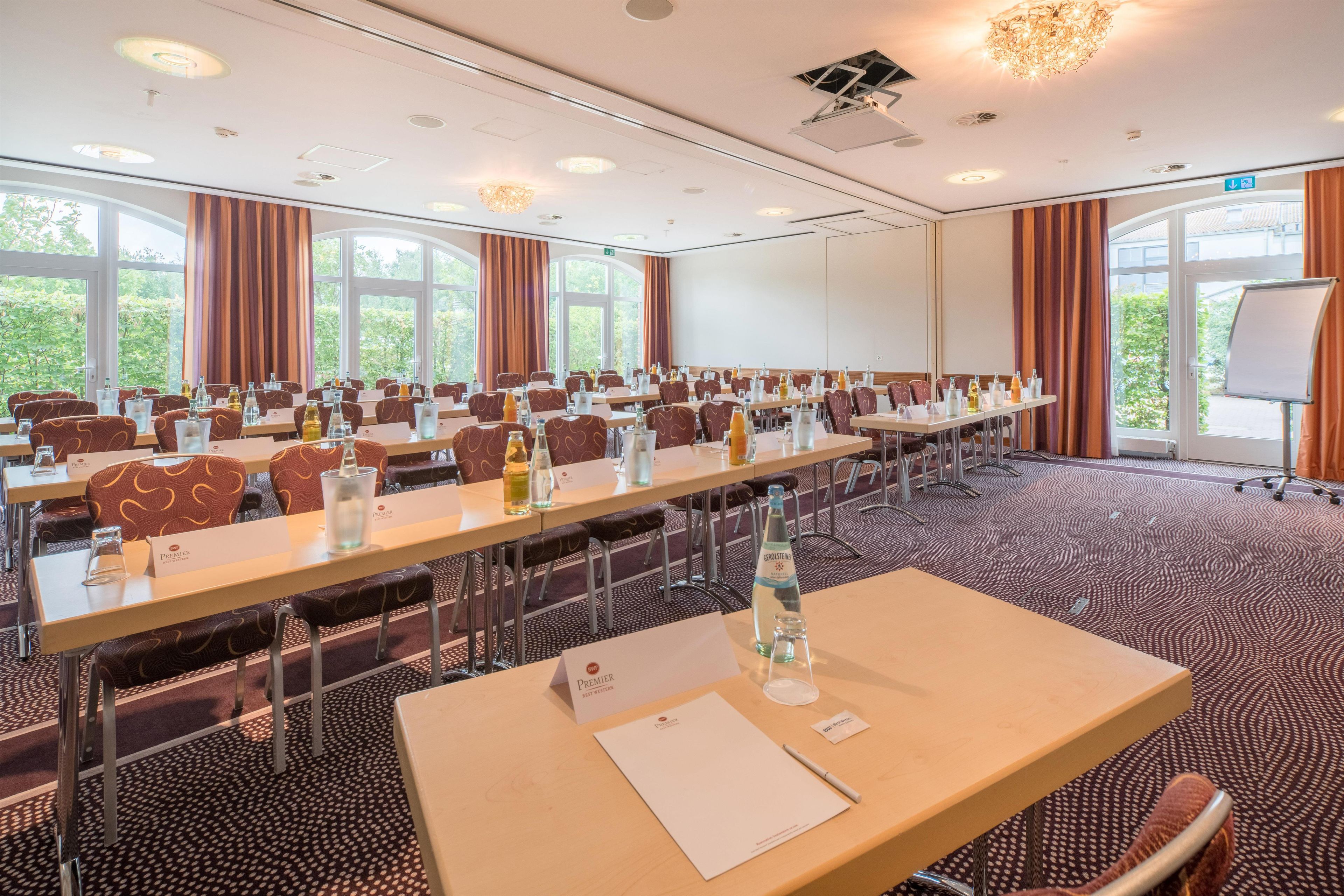 A conference room with long tables, chairs, and nameplates, equipped with water bottles and a projector screen.