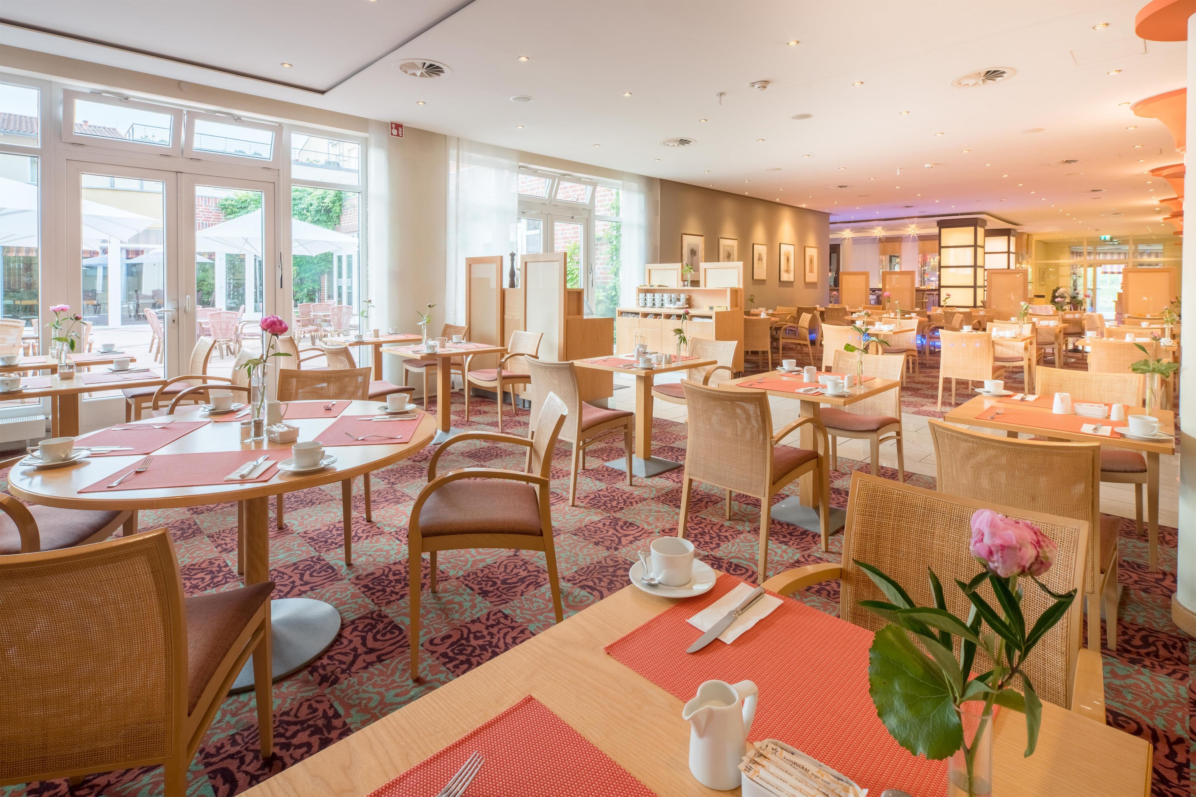 A hotel dining area with multiple tables, chairs, and a view of the outdoors through large windows.