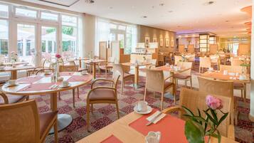 A hotel dining area with multiple tables, chairs, and a view of the outdoors through large windows.