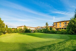 A golf course with a clear sky, surrounded by multi-story buildings with balconies.