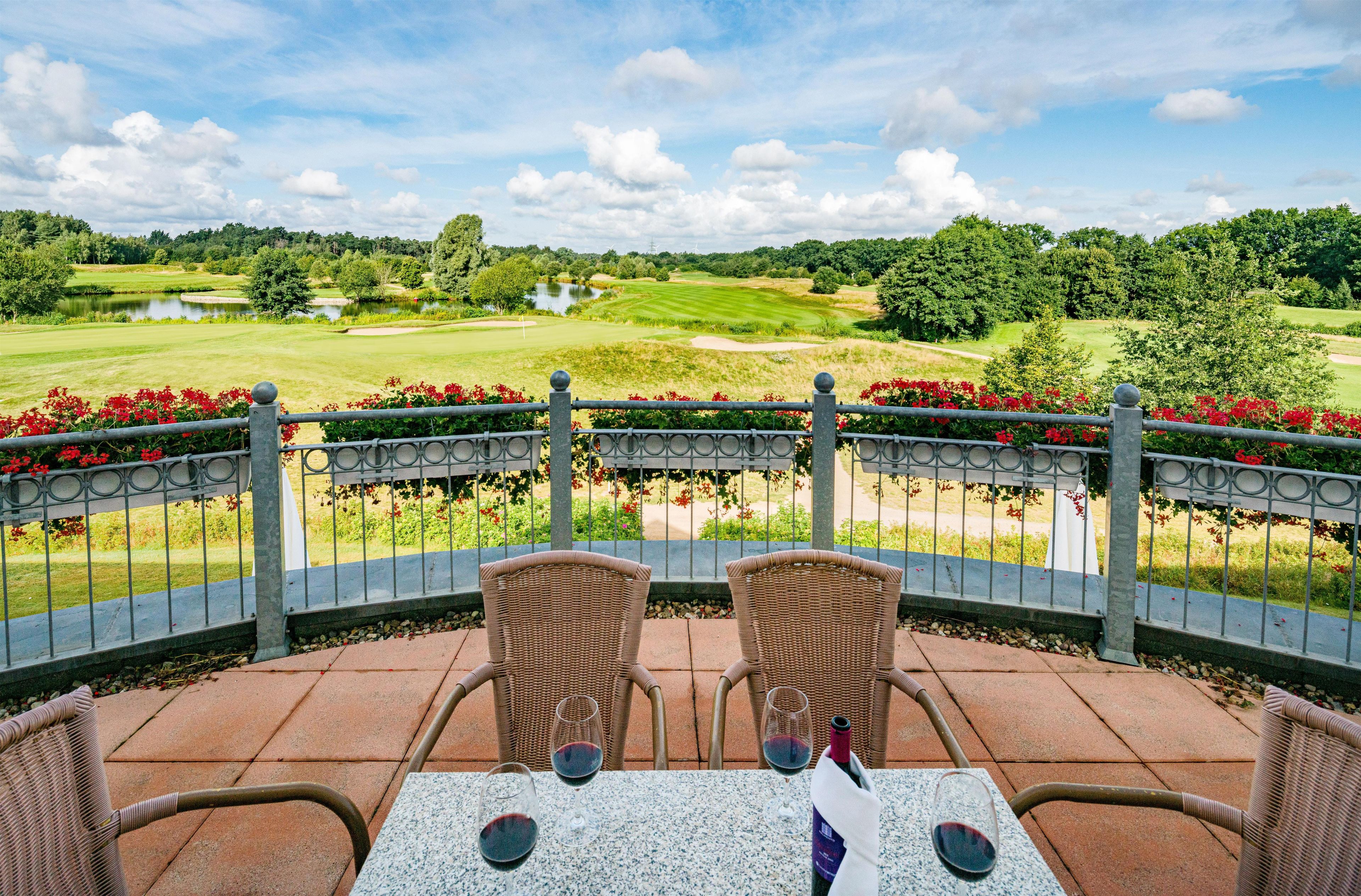 A patio with wicker chairs and a table, overlooking a golf course.