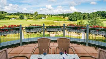 A patio with wicker chairs and a table, overlooking a golf course.