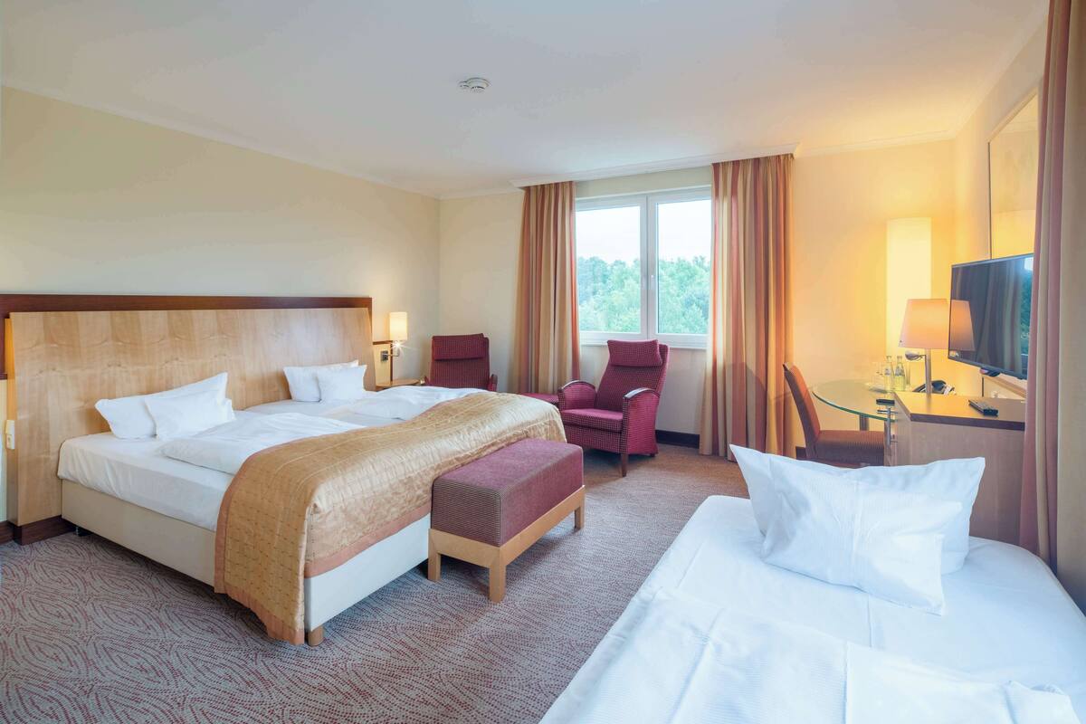 Ein Hotelzimmer mit zwei Betten, einer Sitzecke mit Sessel, einem kleinen Tisch mit Lampe und einem Fernseher.