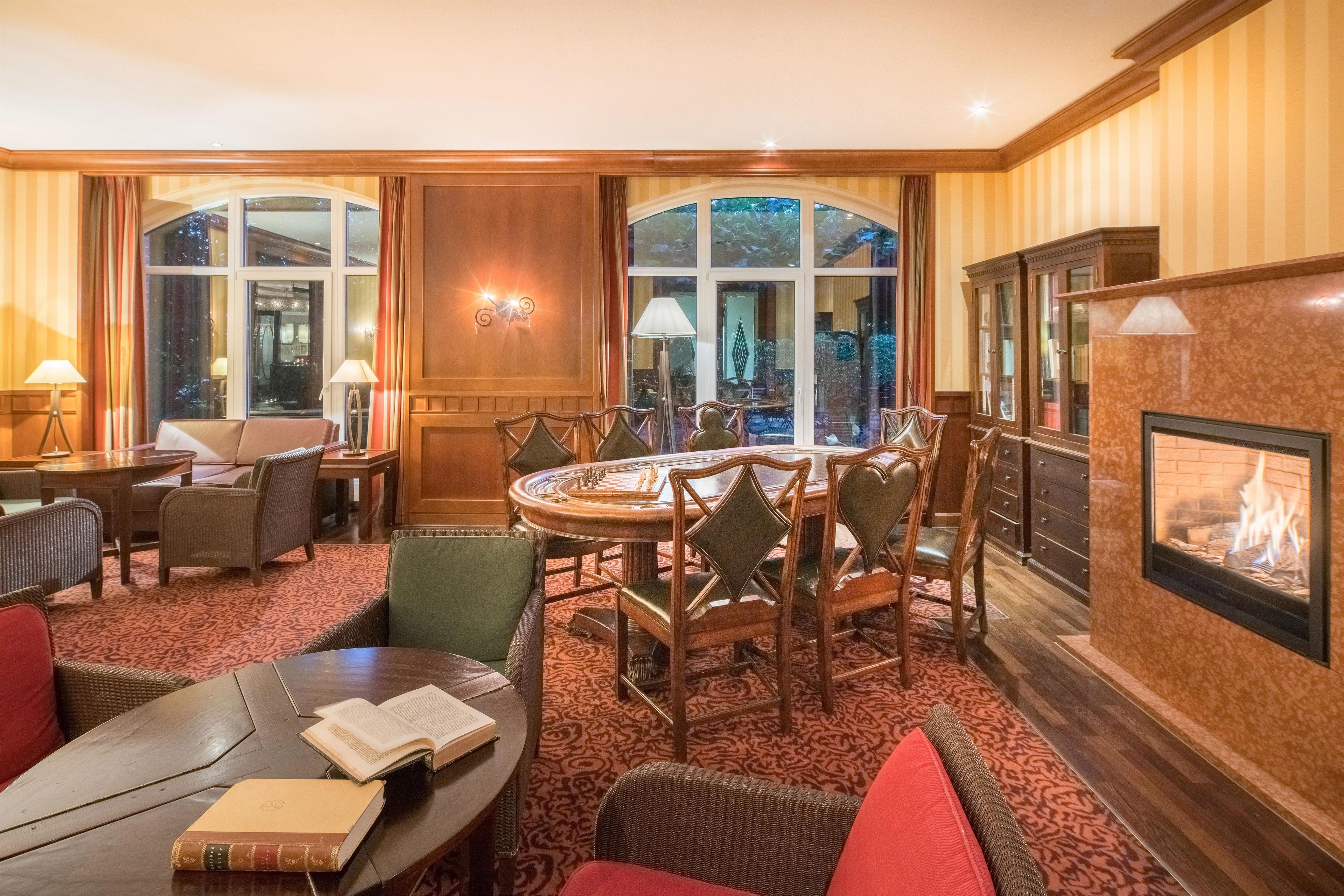 Habitación de hotel con una mesa redonda de comedor, varias sillas, chimenea y ventanas amplias.