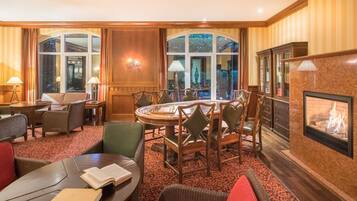 Habitación de hotel con una mesa redonda de comedor, varias sillas, chimenea y ventanas amplias.