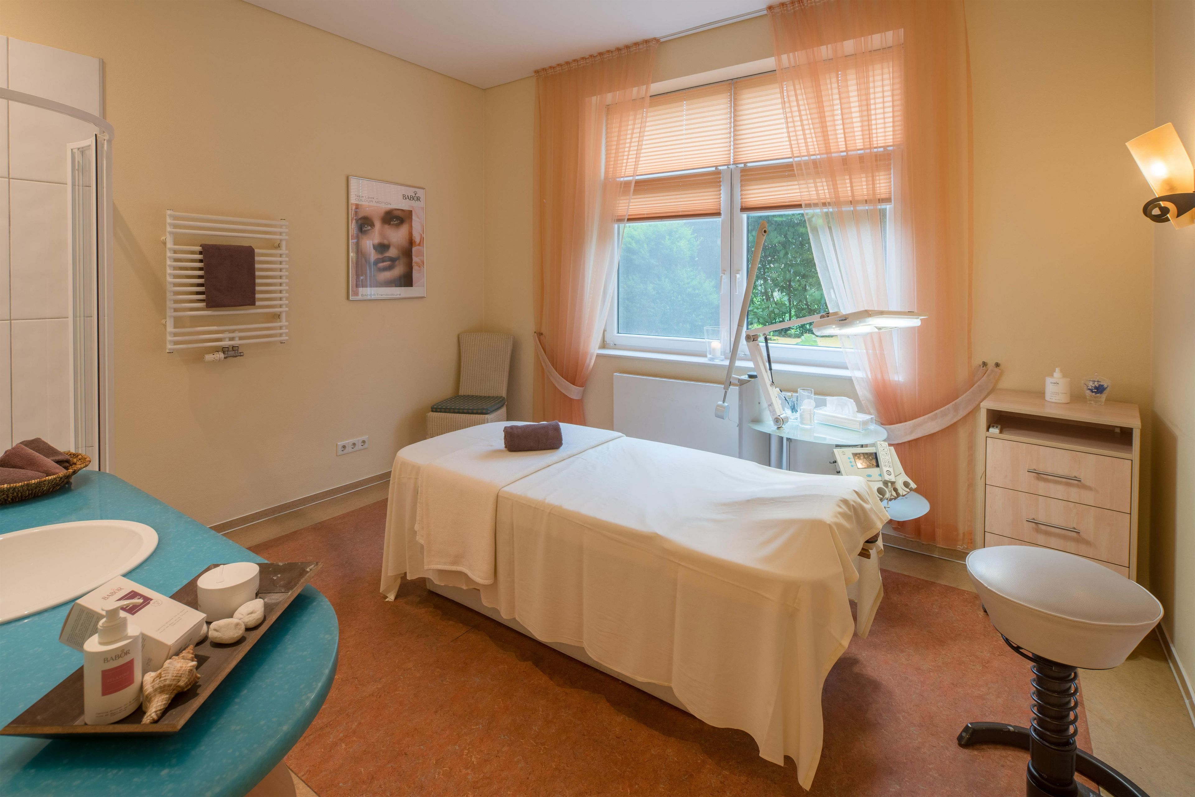 A room with a bed, a window with curtains, a sink, and a small table with toiletries.