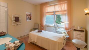 A room with a bed, a window with curtains, a sink, and a small table with toiletries.