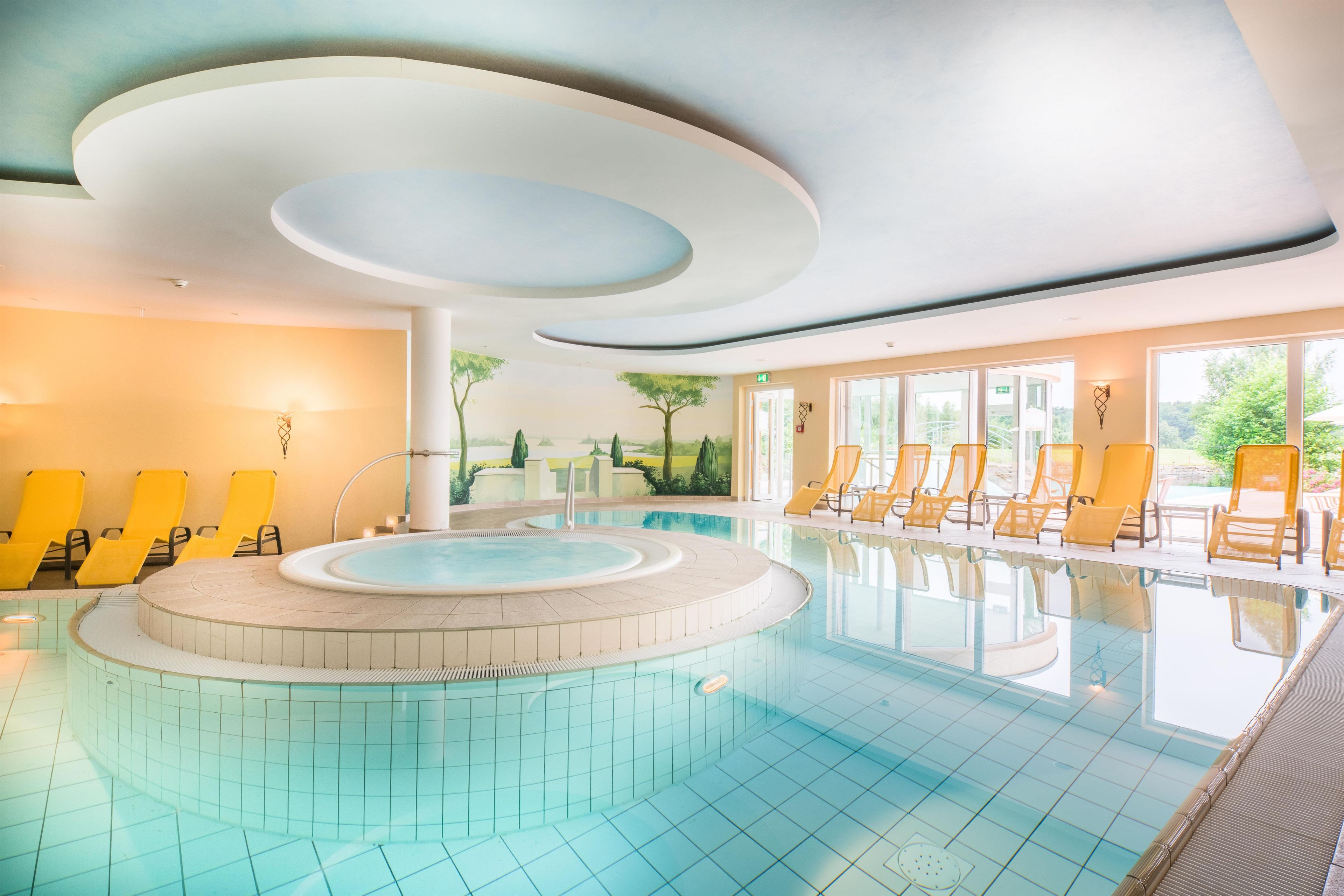 Ein Pool mit kreisförmigem Design, umgeben von gelben Liegestühlen, und ein Wandgemälde mit einer Landschaftsmalerei an der angrenzenden Wand.