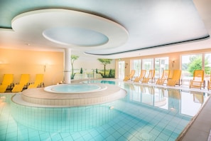 Una piscina con diseño circular, rodeada de sillas de descanso amarillas y un mural que representa un paisaje en la pared contigua.