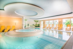Una piscina con diseño circular, rodeada de sillas de descanso amarillas y un mural que representa un paisaje en la pared contigua.