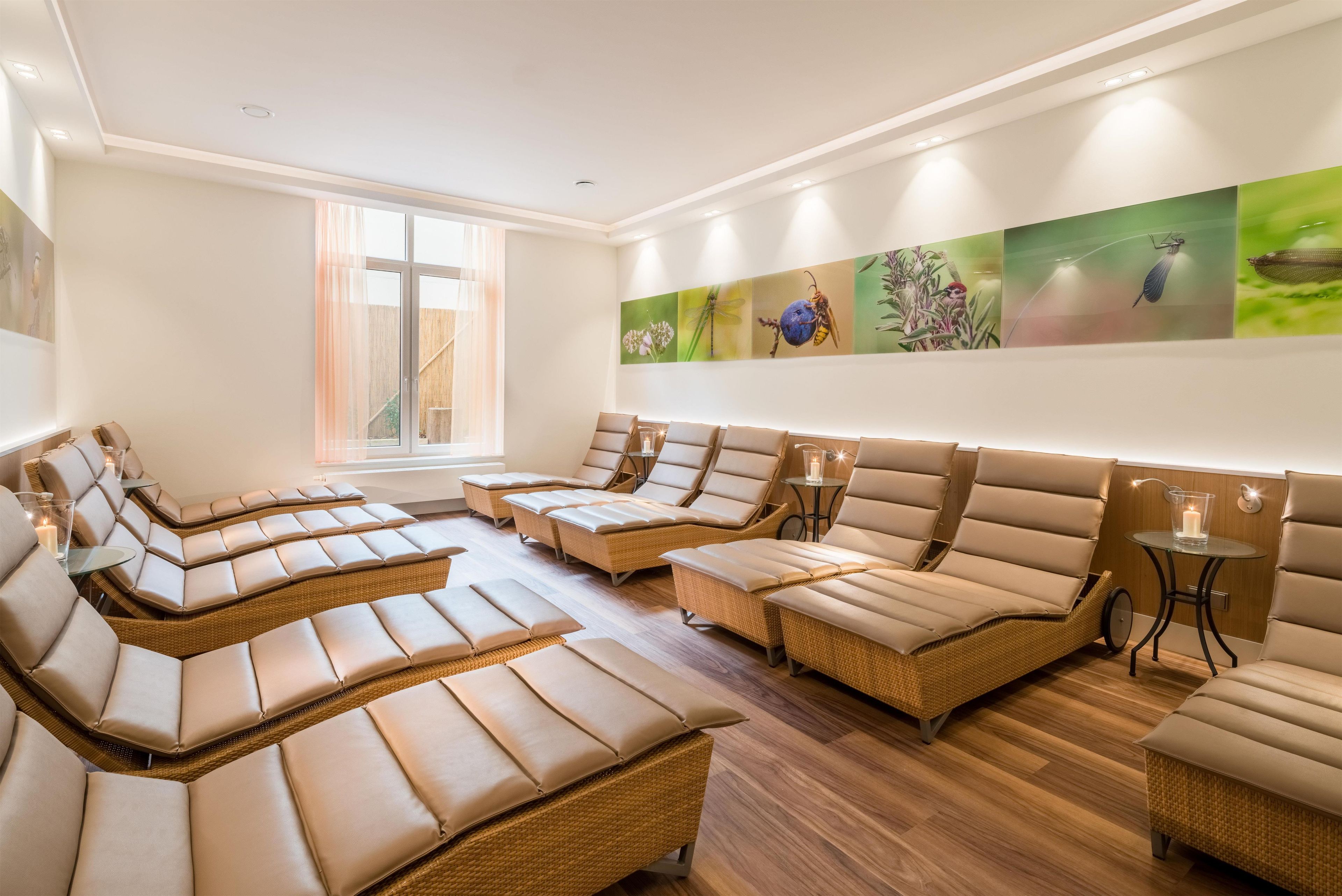 Ein Spa-Raum mit mehreren Liegen für Massagen, die halbkreisförmig angeordnet sind, einem großen Fenster für natürliches Licht und einer Wand mit naturbezogenen Kunstwerken.