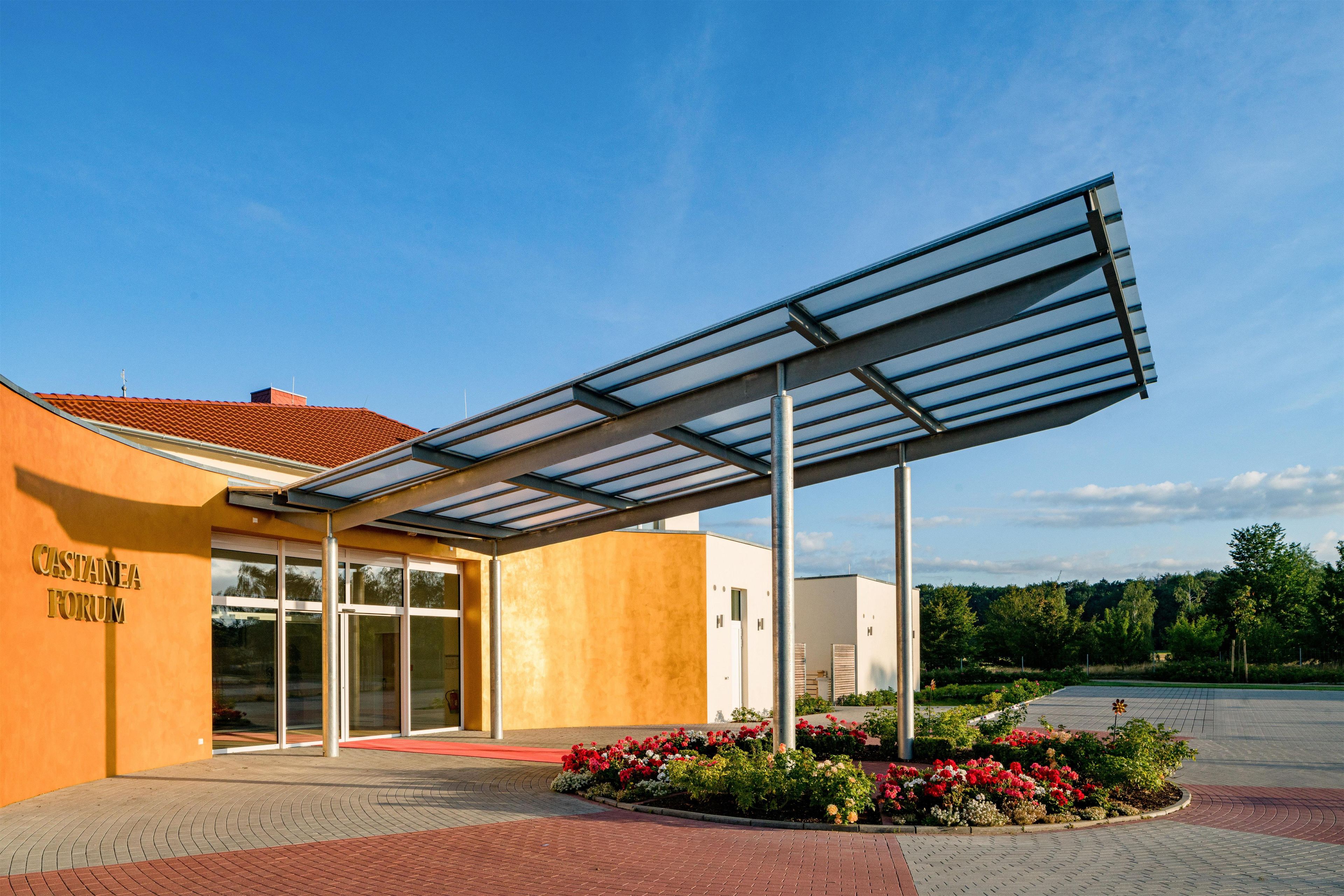 A building with a covered entrance, a sign reading 'CASTANEA FORUM,' and a landscaped area with flowers.